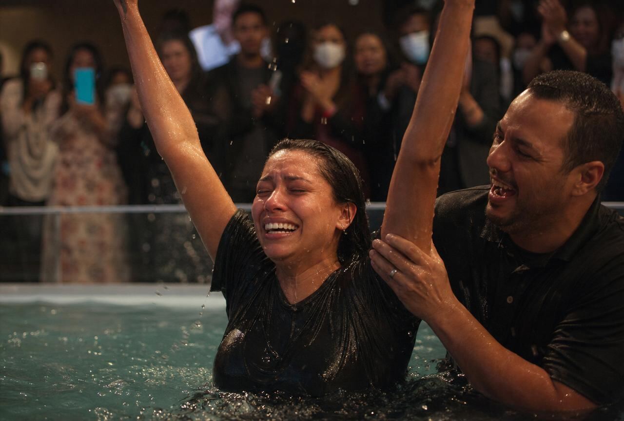 New believer emerging from baptism waters, arms raised in joy